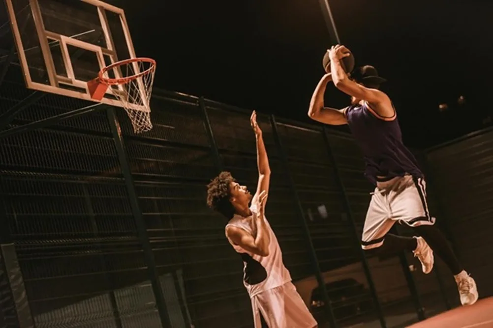 Jóvenes jugando baloncesto en una cancha urbana durante la noche.