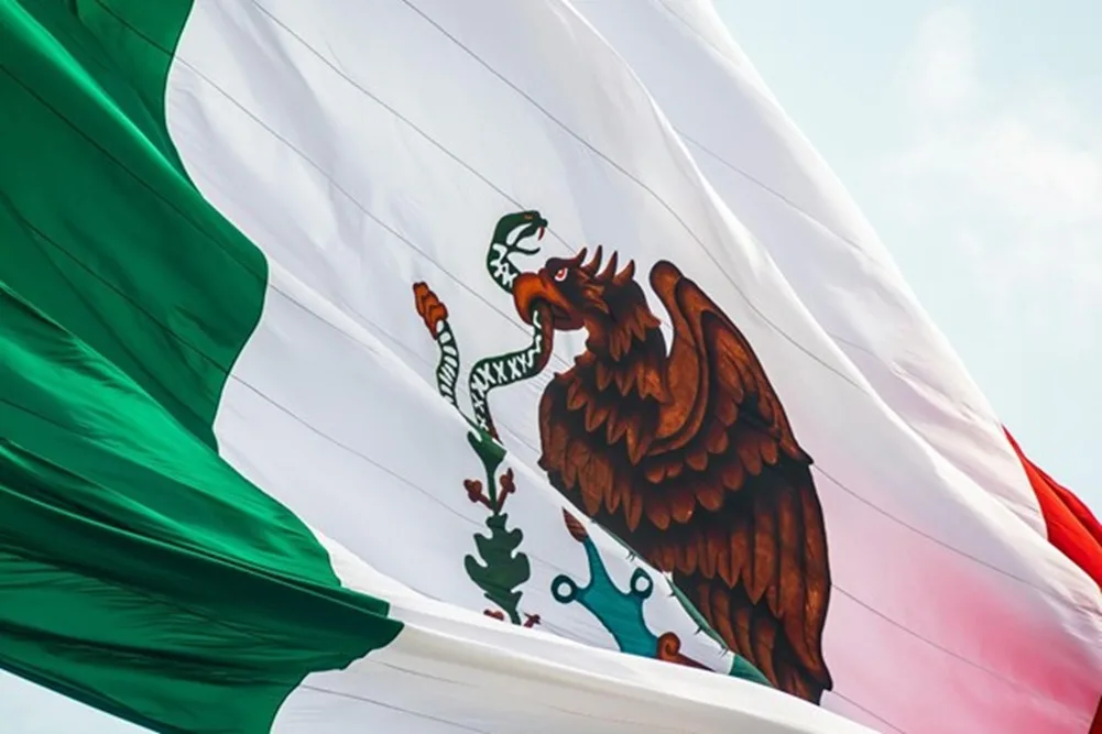 Bandera nacional de México flameando al viento con el escudo del águila y la serpiente en primer plano.